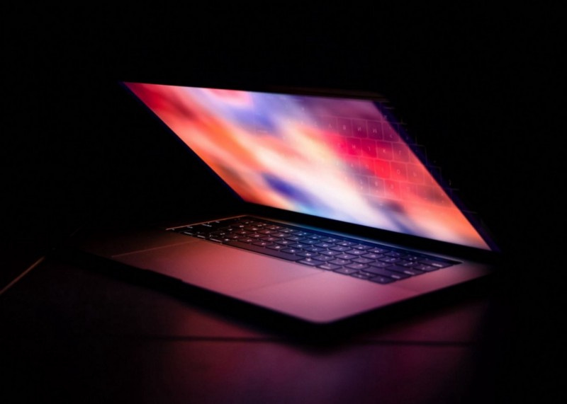 Um notebook da apple com a tela em proteção de tela, com tela meio fechada, e pouca iluminação
