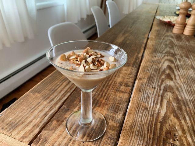 A cocktail glass with a brown liquid in it and chopped almonds on top