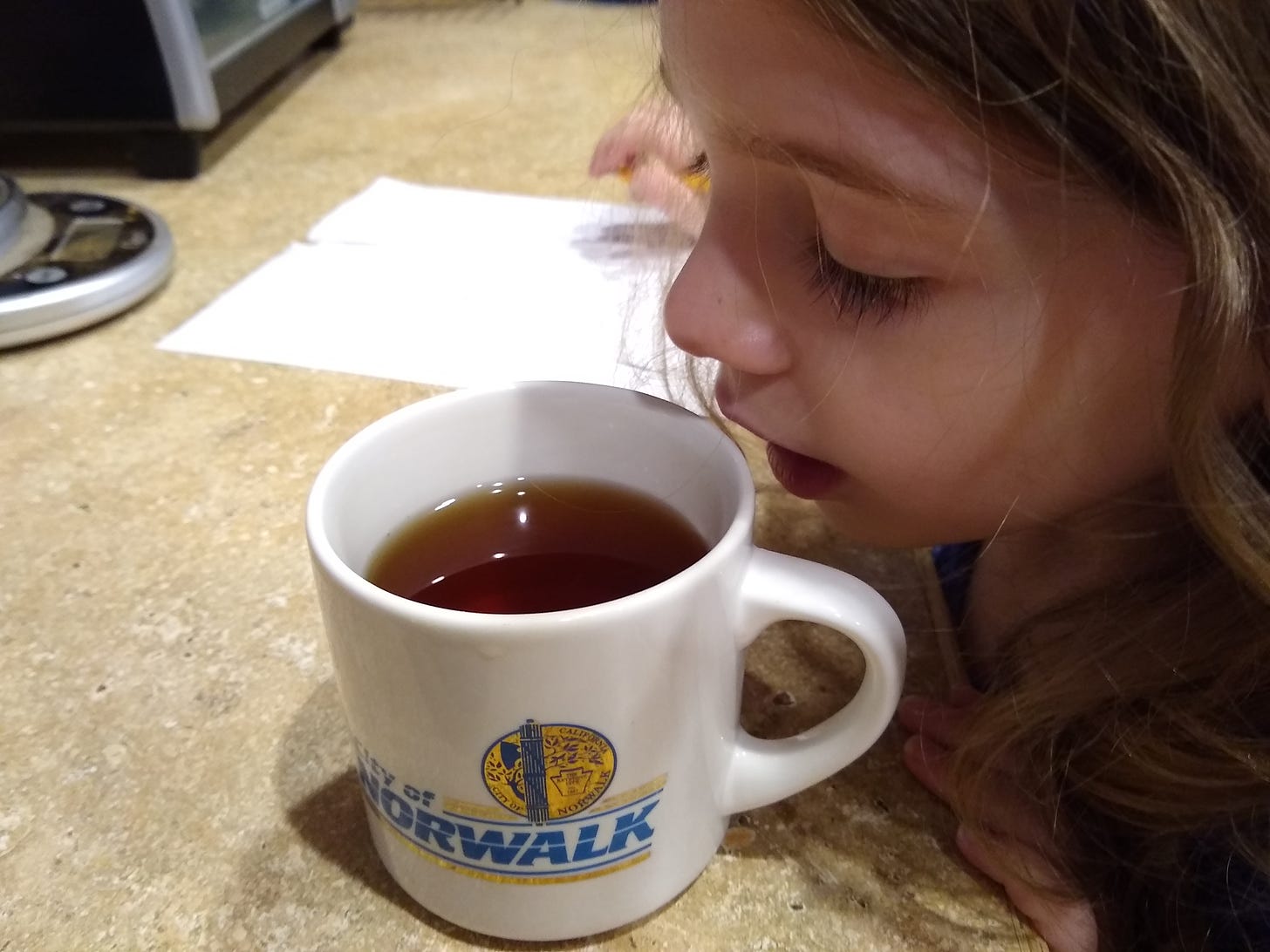 A child's face hovering over a hot beverage