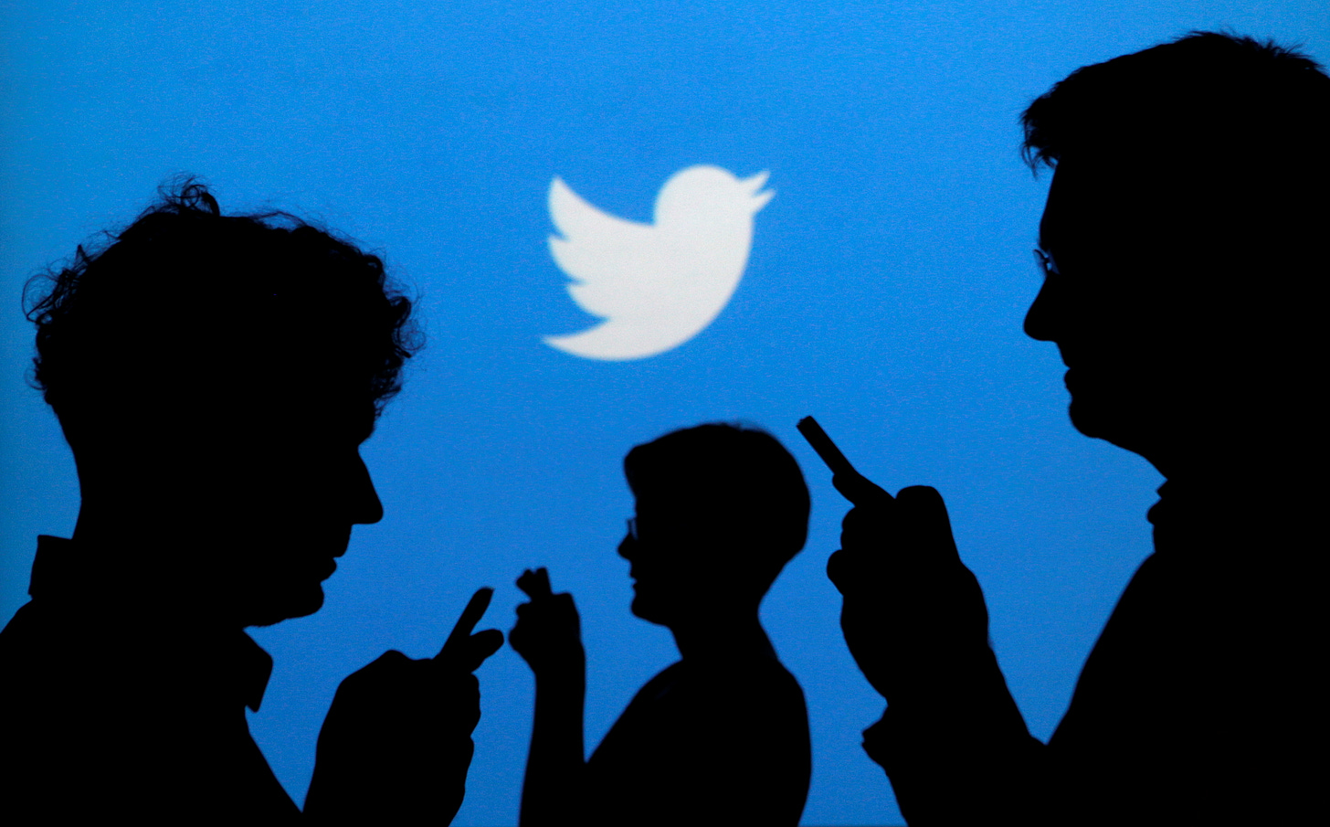 People holding mobile phones are silhouetted against a backdrop projected with the Twitter logo in this illustration picture taken in  Warsaw September 27, 2013.  REUTERS/Kacper Pempel/File Photo