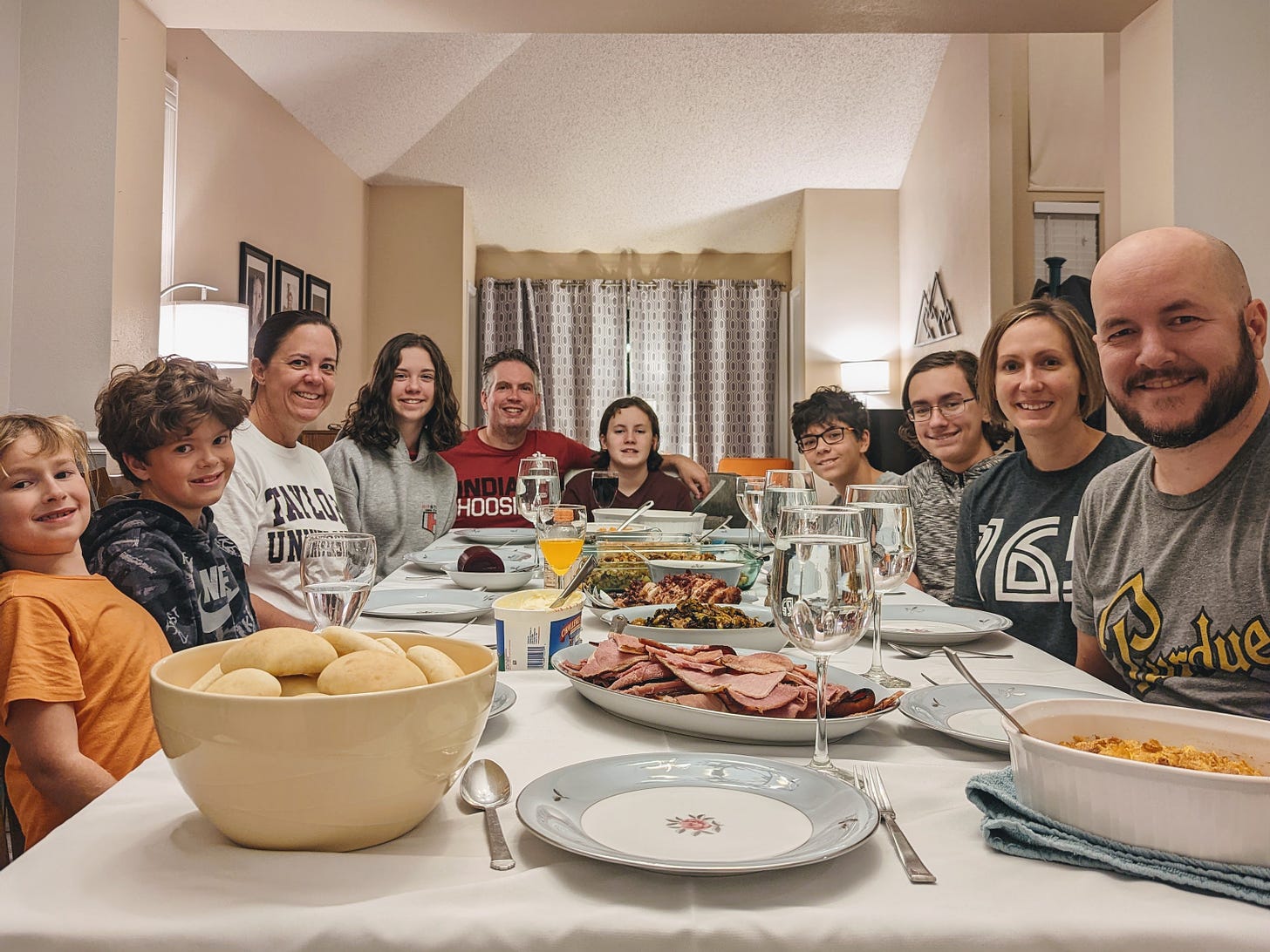 A table full of food is surrounded by 10 family members, smiling at the camera.