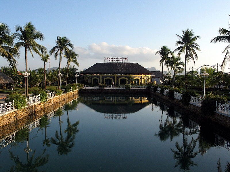 File:Tuần Châu island. The image shows a low pavilion surrounded by palm trees. A long reflecting pool is in front of the pavilion, showing a reflection of the pavilion. Low hills are visible in the background as well as other buildings with similar thatched roofs. File:Tuần Châu island. The image shows a low pavilion surrounded by palm trees. A long reflecting pool is in front of the pavilion, showing a reflection of the pavilion. Low hills are visible in the background as well as other buildings with similar thatched roofs.