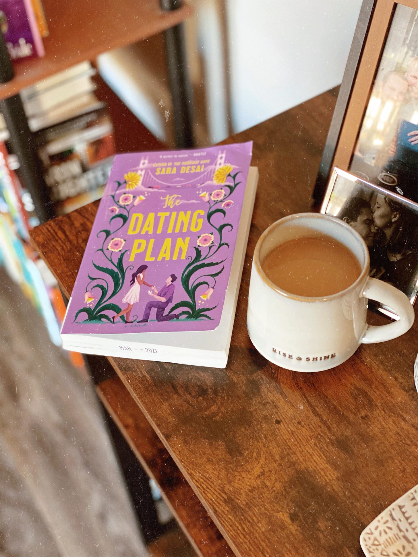 A photo of The Dating Plan sitting on a dark wood coffee table. A cup of coffee is set down to the right of the book. The book cover is a light purple, with yellow lettering.