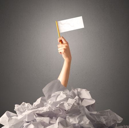 A female hand rising from a pile of screwed up paper, waving a white flag