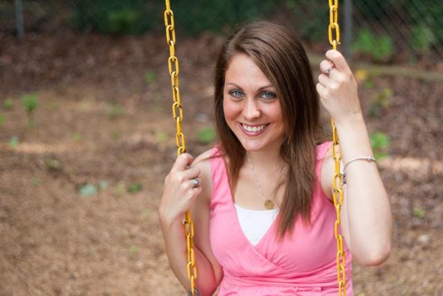 a photo of Kendra at 22. She’s a white woman with brunette hair sitting in a swing smiling at the camera