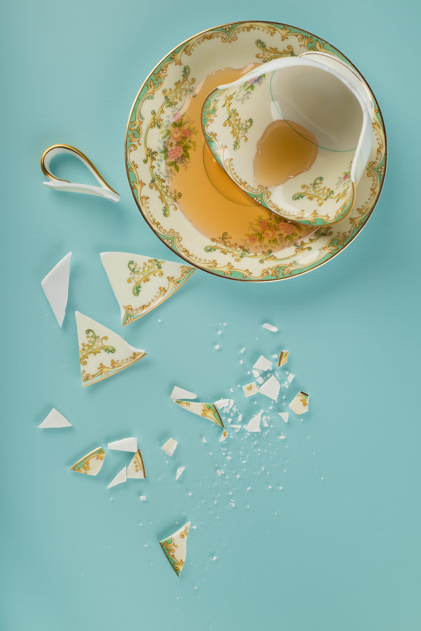 A dainty shattered teacup leaking tea onto the saucer