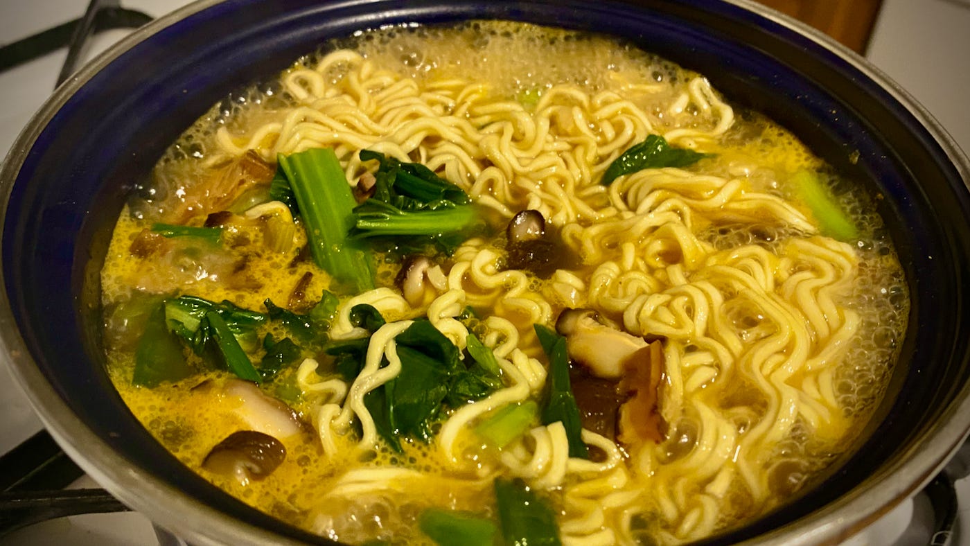 A pot on my stove with boiling broth, ramen noodles, Chinese greens, scallions, and shiitake mushrooms