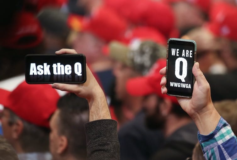 People hold up phones with the letter Q on them