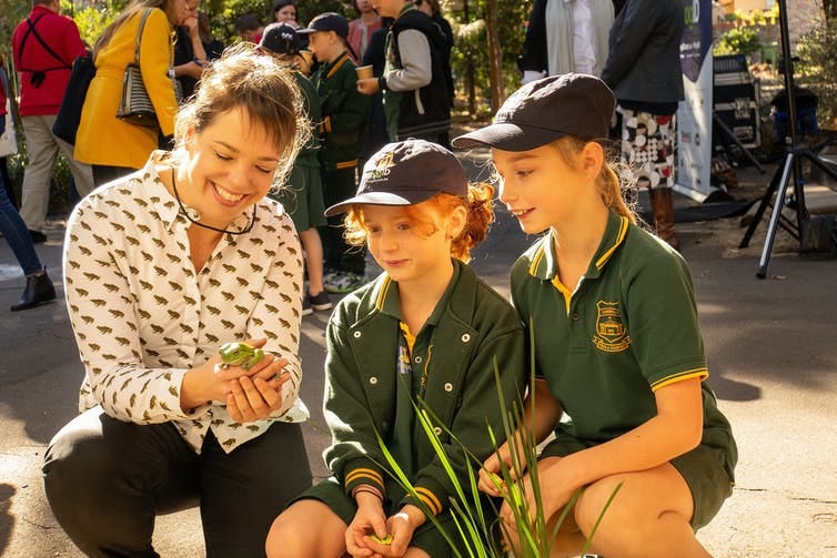 woman shows frog to school students