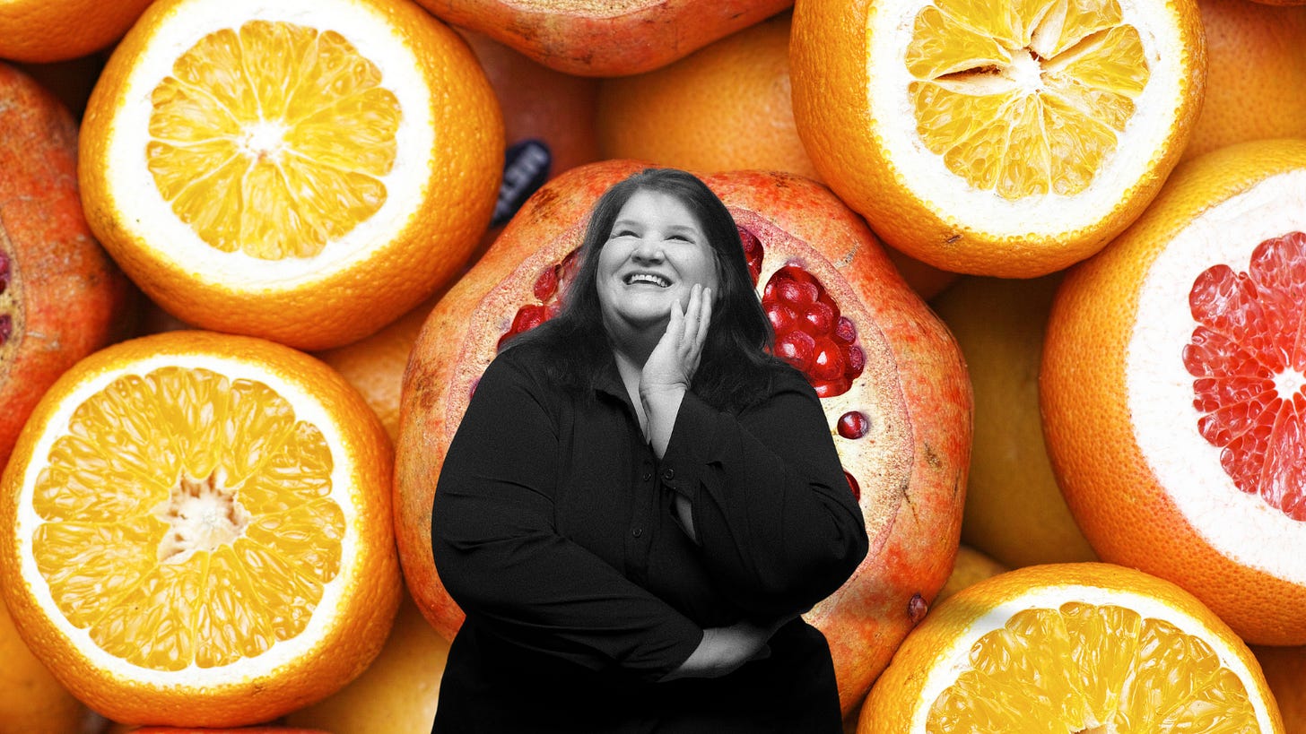 A woman with her arms folded, one hand against her cheek, smiling and looking up, on a background of citrus slices