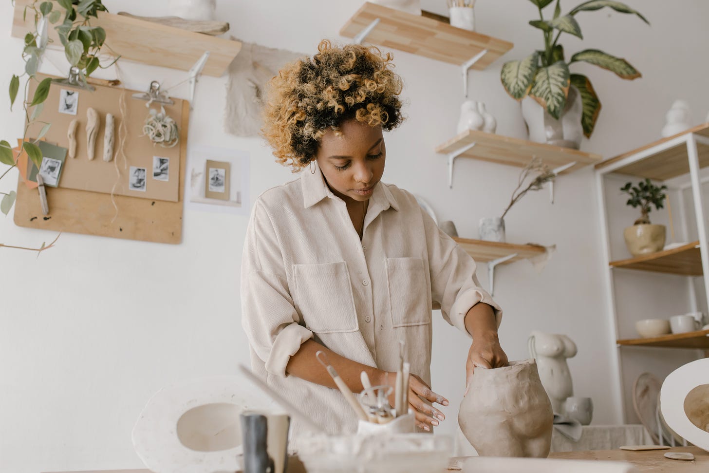 A woman moulding clay in a room with clay and shelves behind her