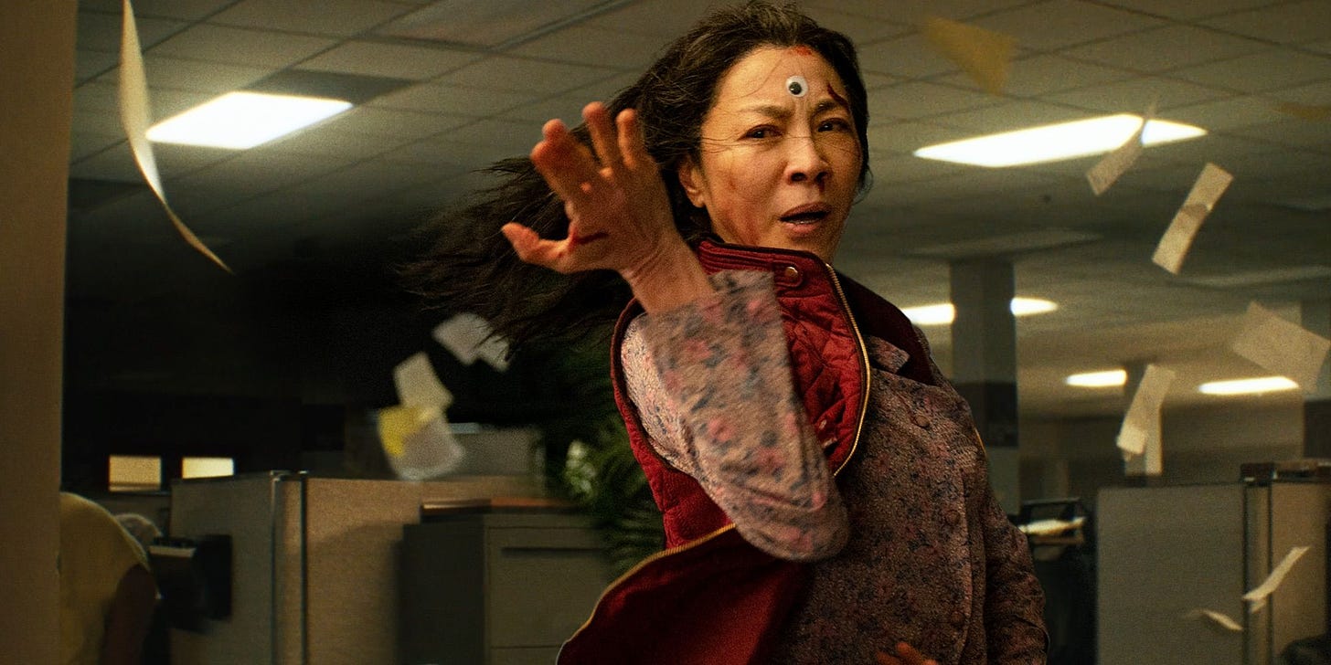 Michelle Yeoh with a googly eye in the middle of her forehead strikes a kung fu post in an office as papers are blown in the air around her