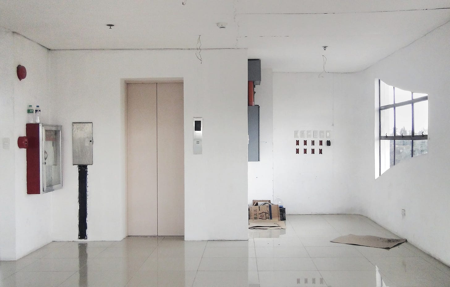imagem mostra apartamento vazio, branco, com porta de elevador fechada.