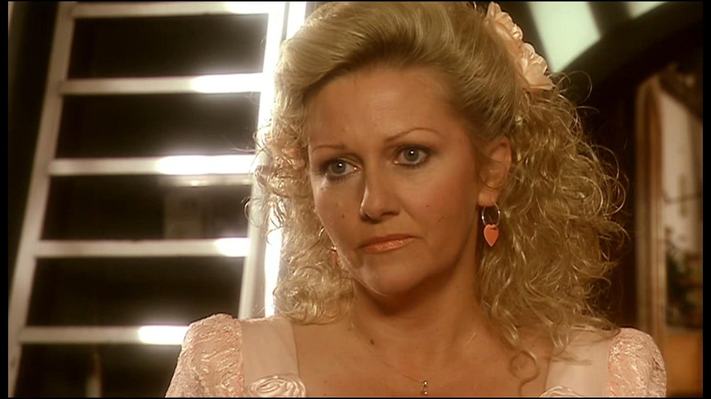 This image shows Jackie Tyler (played by Camille Coduri) staring with concern at something off-camera. Jackie wears a wedding dress and sports a perm appropriate for the year 1987.