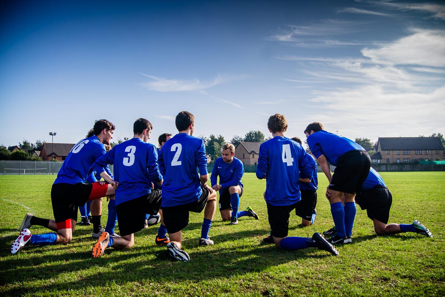 A soccer team wearing blue jerseys kneeling together in a circle. 