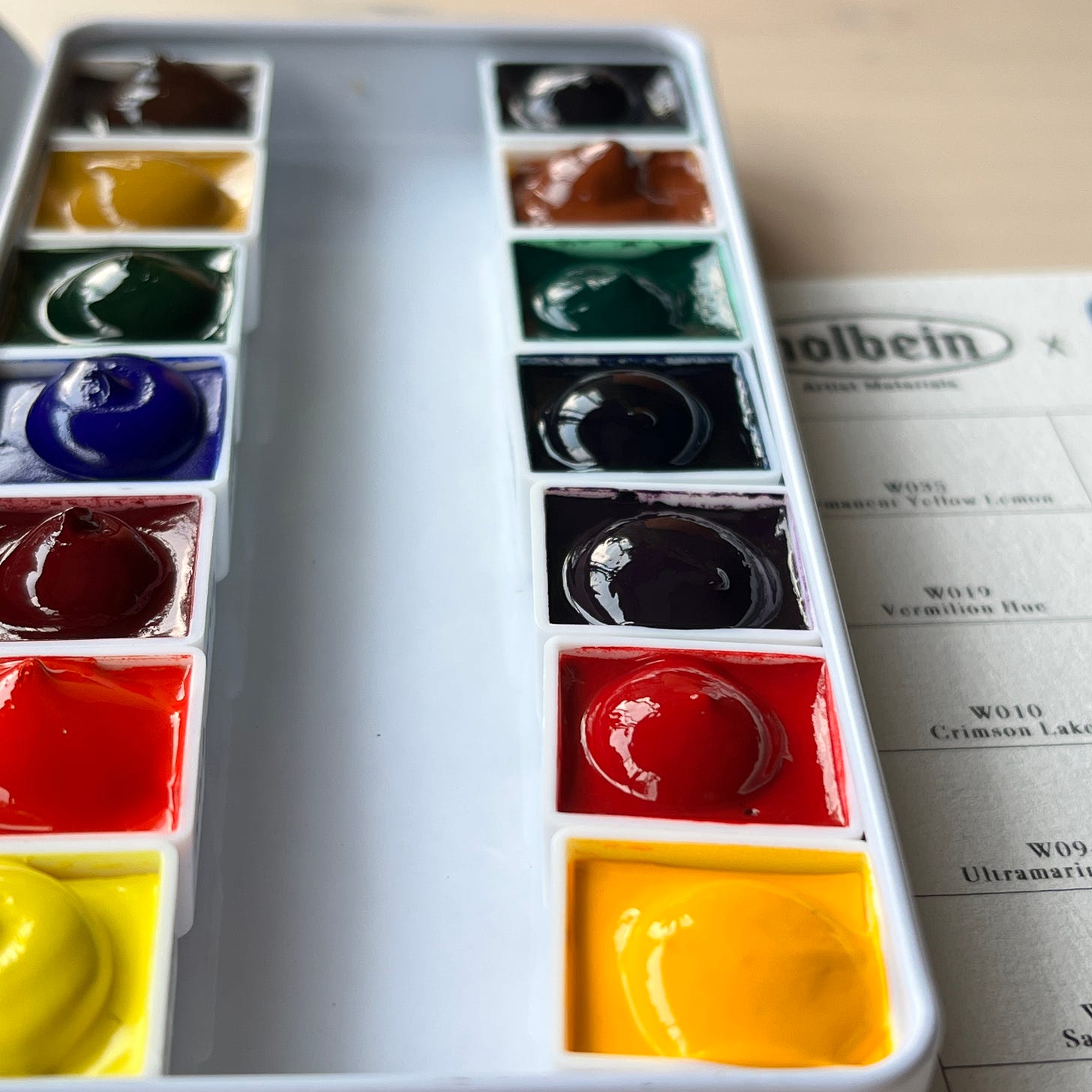image: a set of 14 half-pan watercolour paint set in an enamel travel-sized case from Holbein, a reputable watercolour manufacturer.