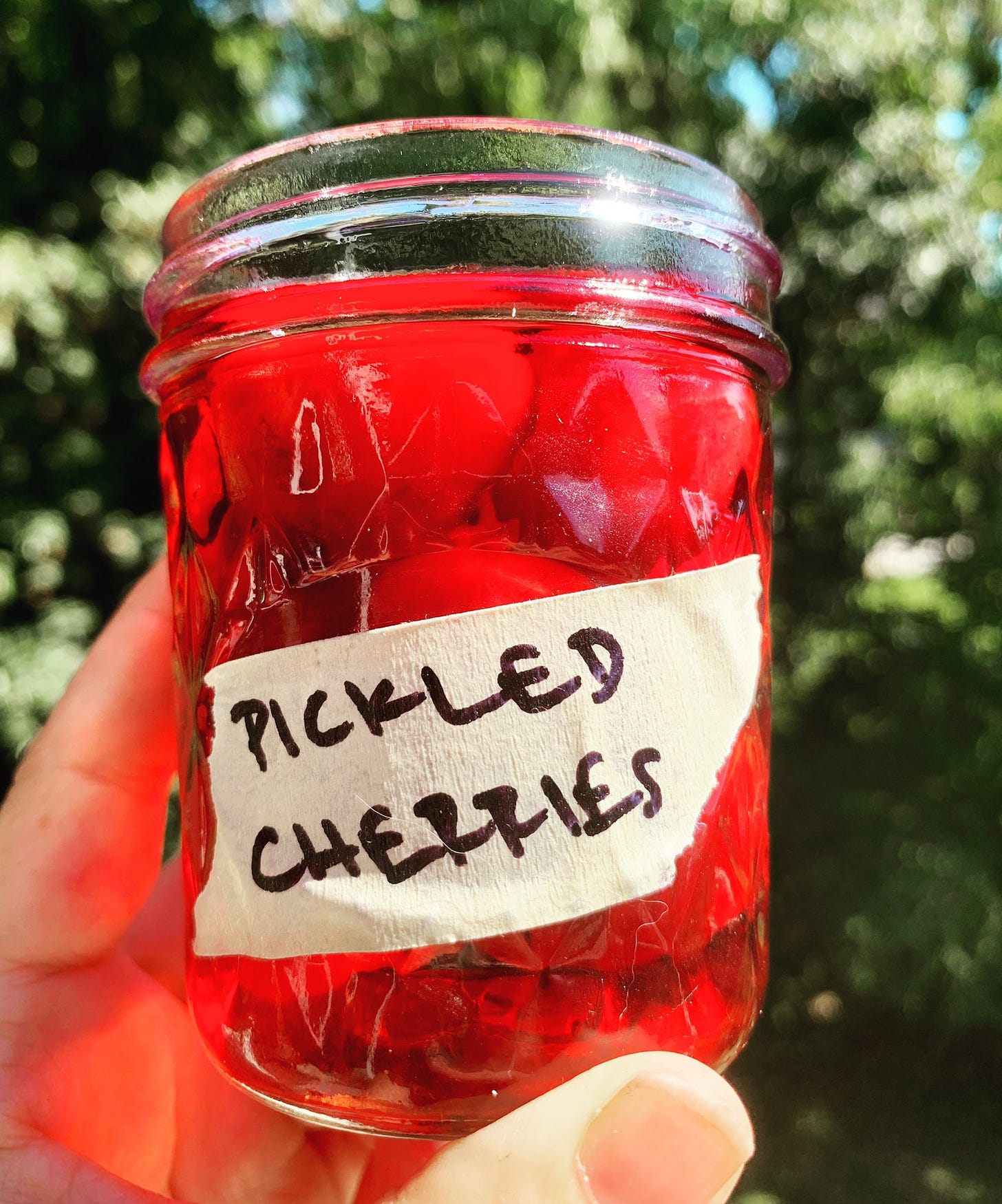 a small mason jar labeled pickled cherries full of bright red cherries