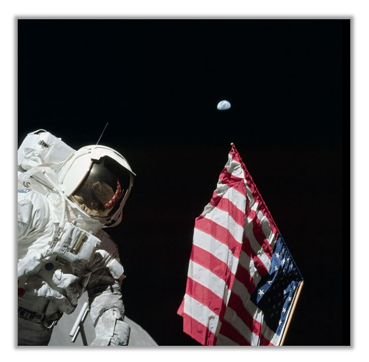 Astronaut Harrison "Jack" Schmitt stands on the moon beside an American flag. Earth is visible in the distance.