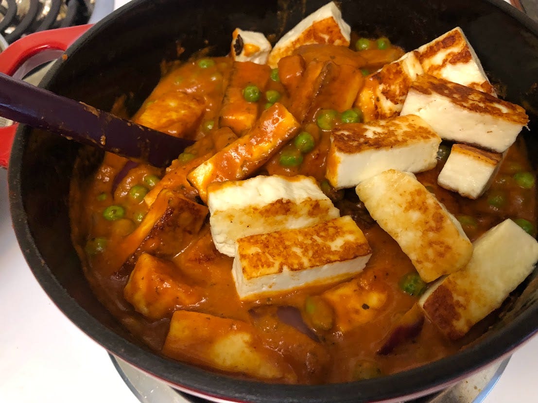 A closer look at the paneer being stirred into the sauce with onions and peas. 