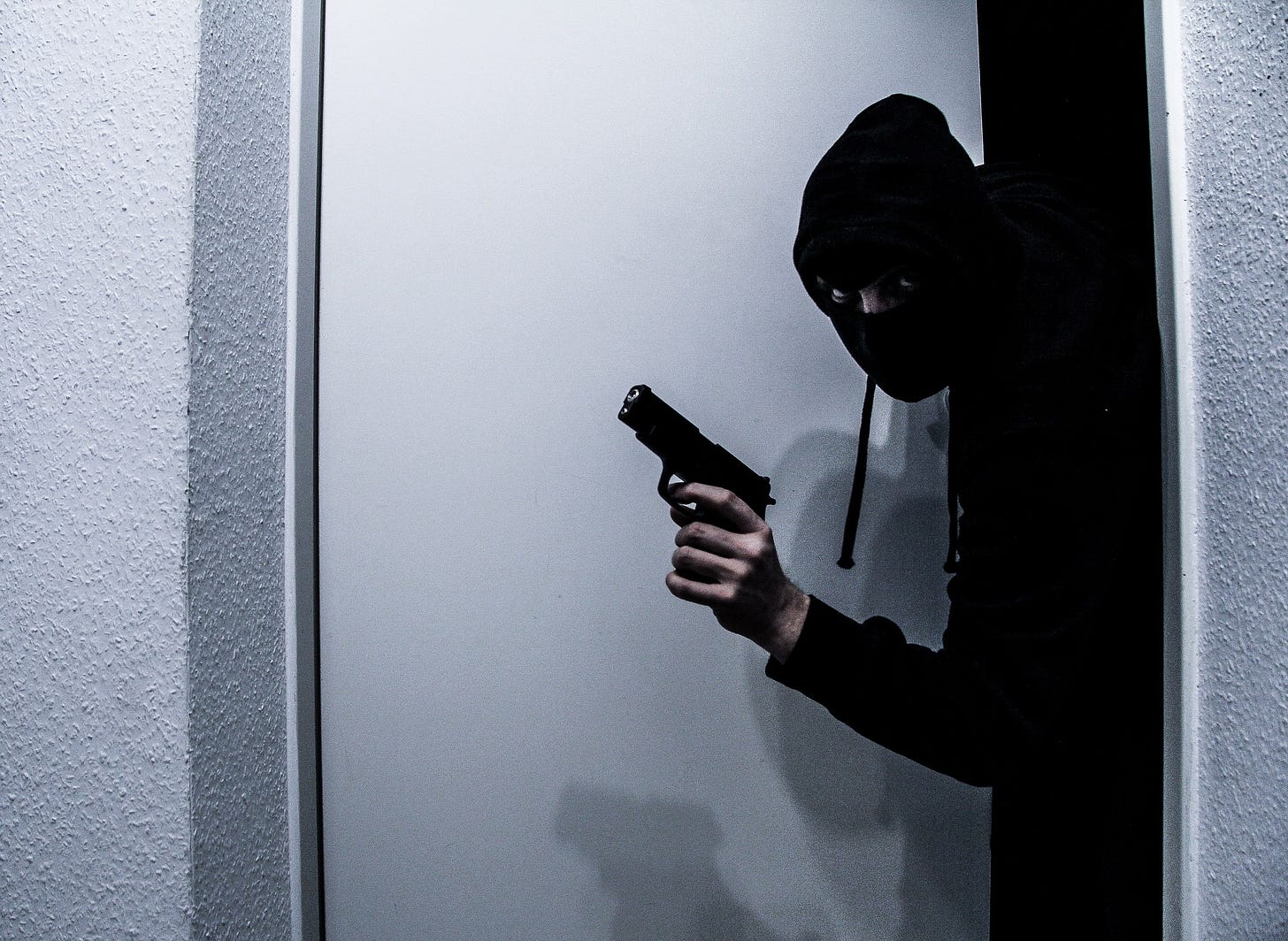 A burgler with a gun exits a doorway.
