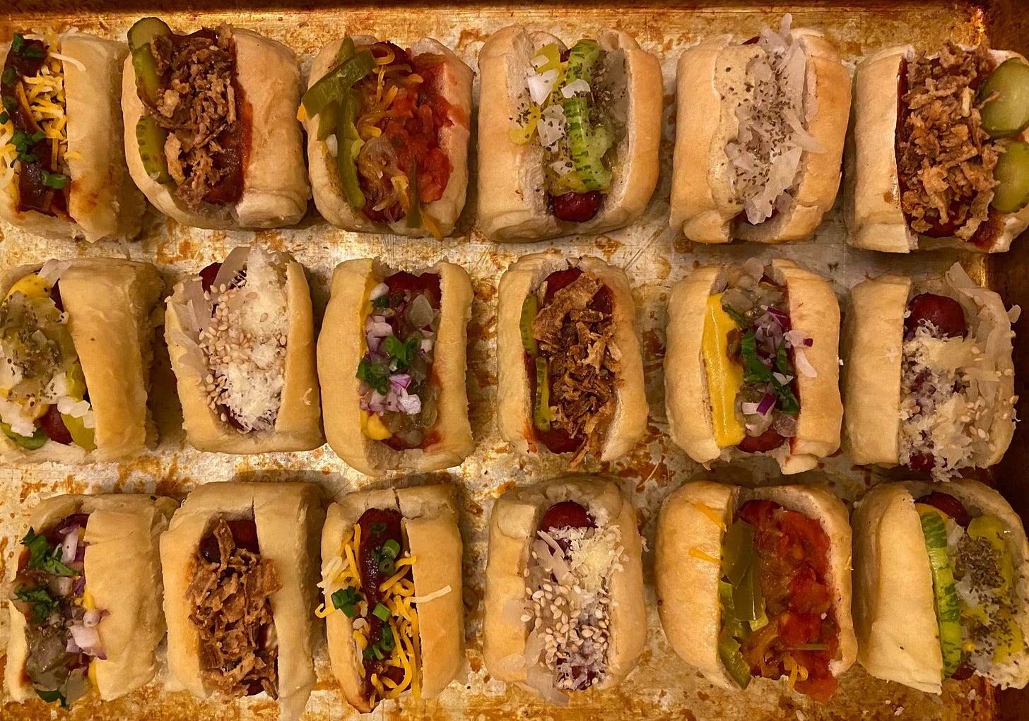 Eighteen miniature hot dogs arranged in three rows with an array of different toppings. 