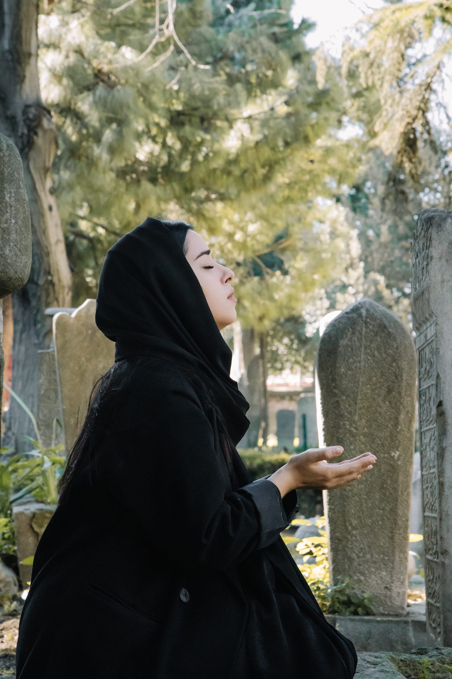 Muslim woman in black praying at a cemetary