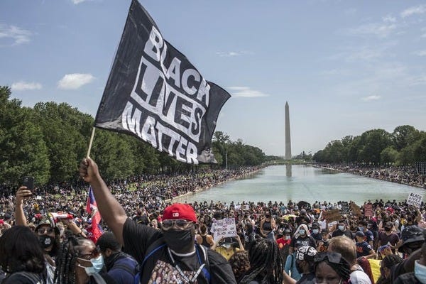 Huge protest at the National Mall in Washington. A man in the front holds a Black Lives Matter flag.