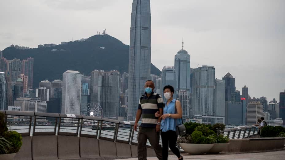 People wearing face masks walks in front of the Hong Kong skyline on October 17, 2022 in Hong Kong, China.