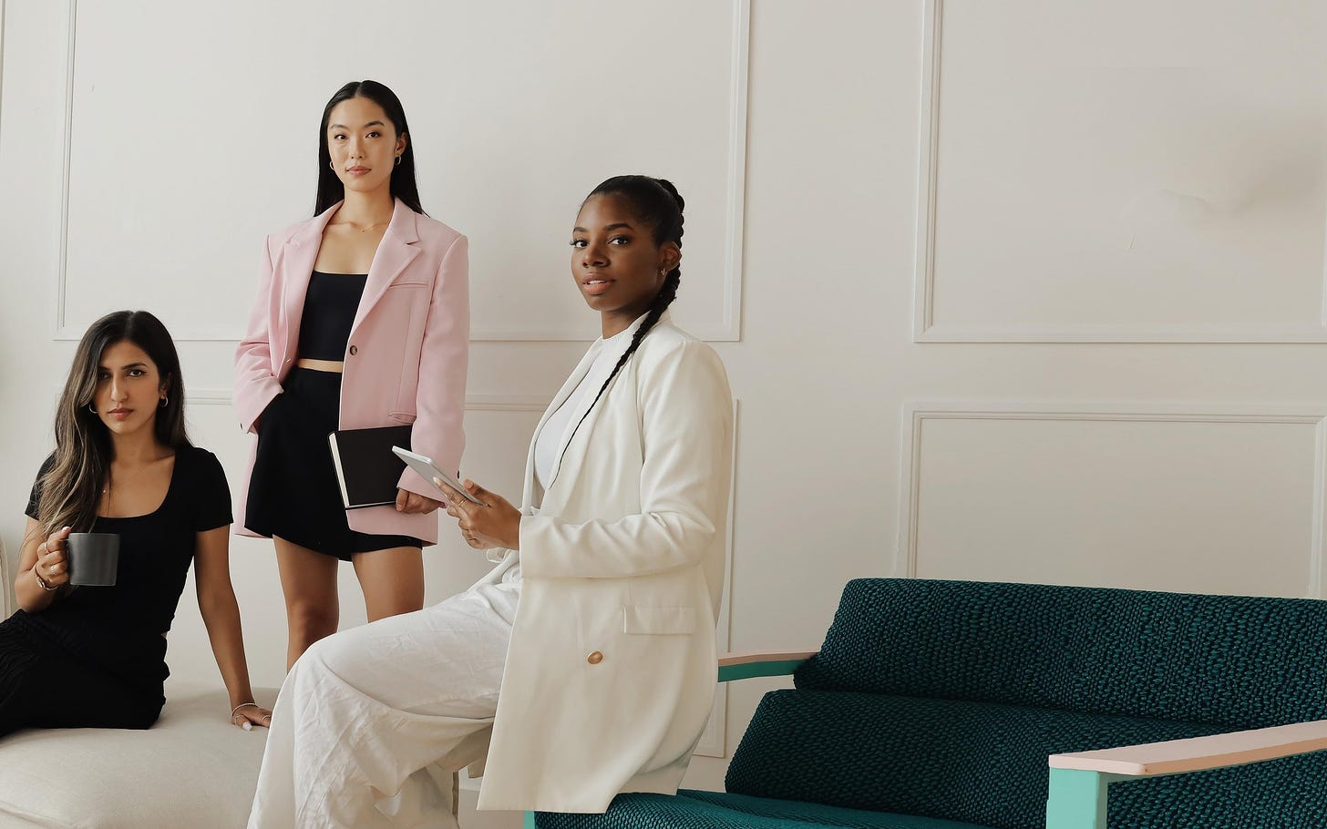 Three women who are dressed professional in front of a white wall. 