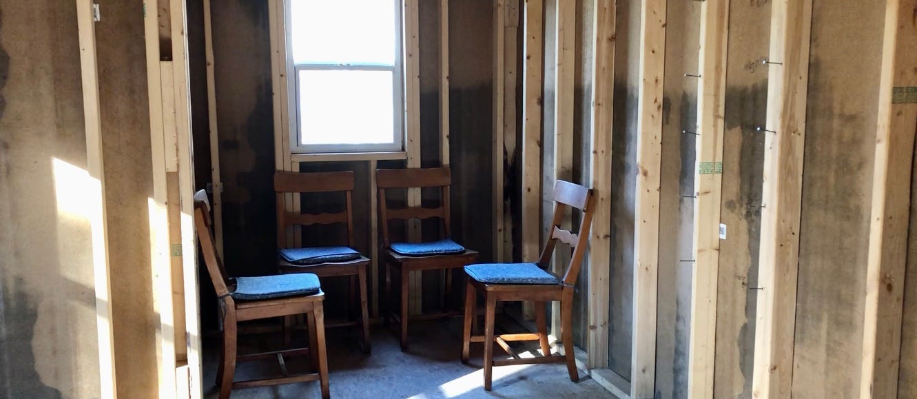 four empty chairs in an empty and unfinished room where sunlight blanks one window above them