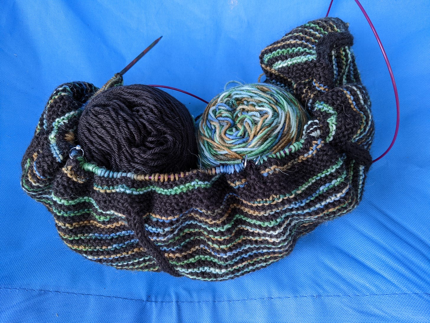 A half-knit scarf in brown and variegated yarn on a blue background