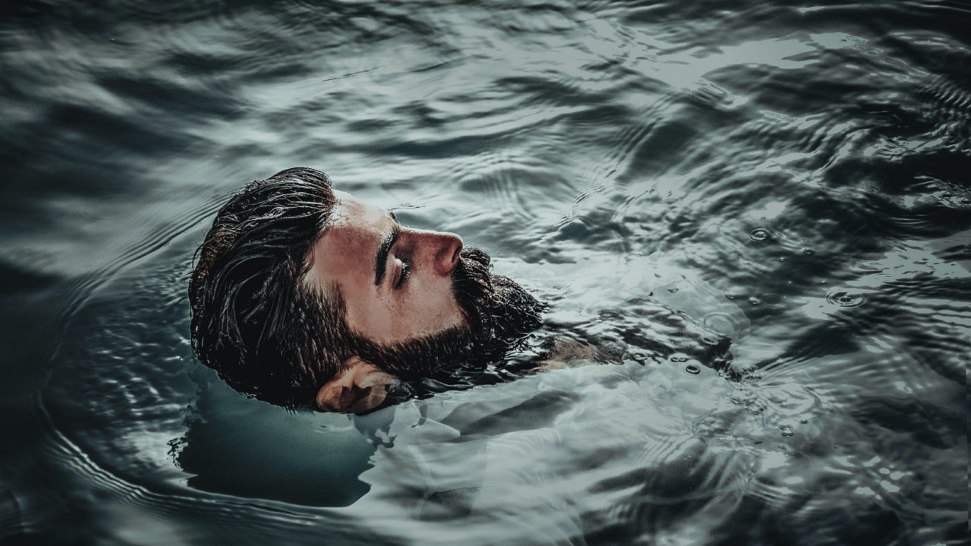 Bearded man immersed in water with only the face above the surface