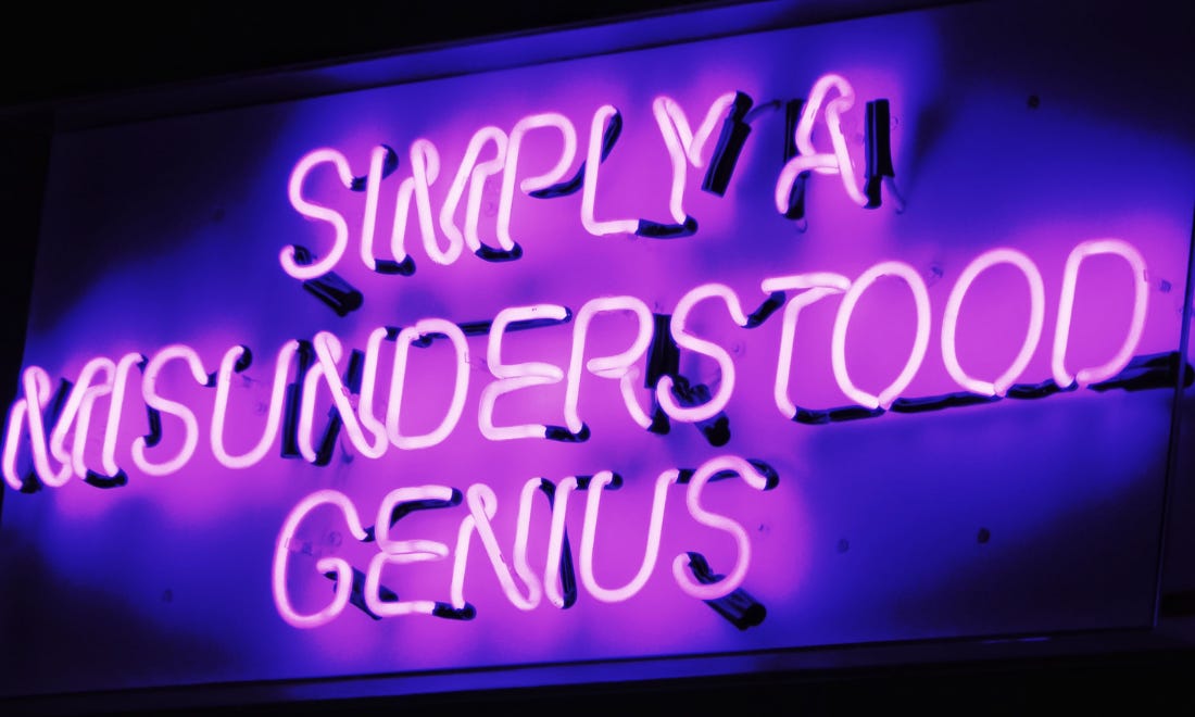 Pink neon sign reads “simply a misunderstood genius”. 