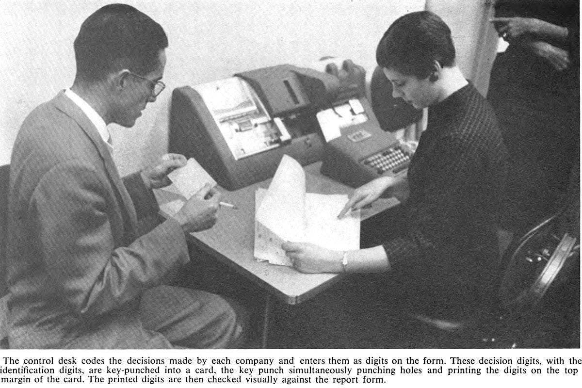 A woman operator seated at a keypunch machine compares a printout with the numbers on a punch card held by a male compatriot.