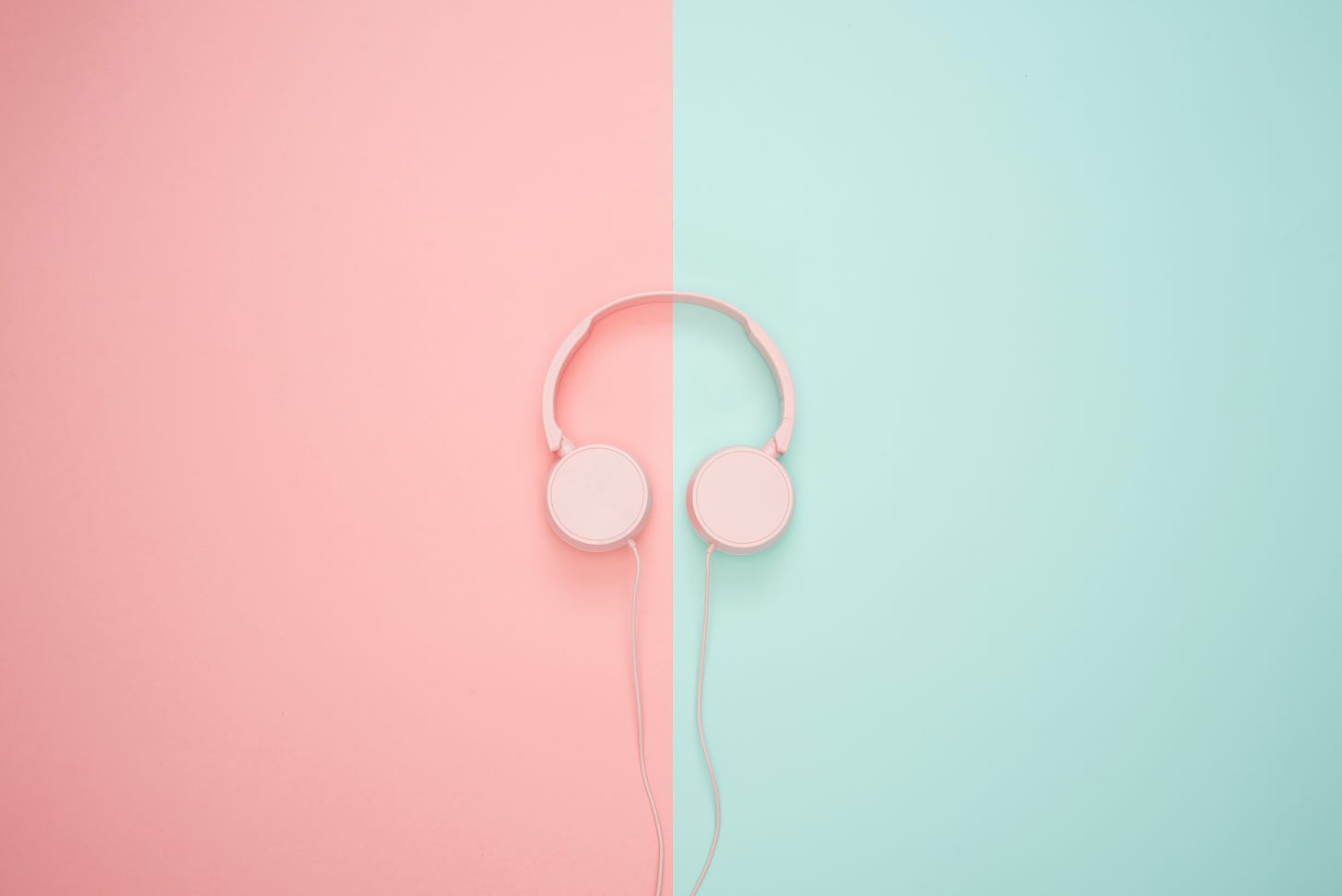 A stock image of pink headphones on a pink and mint green background