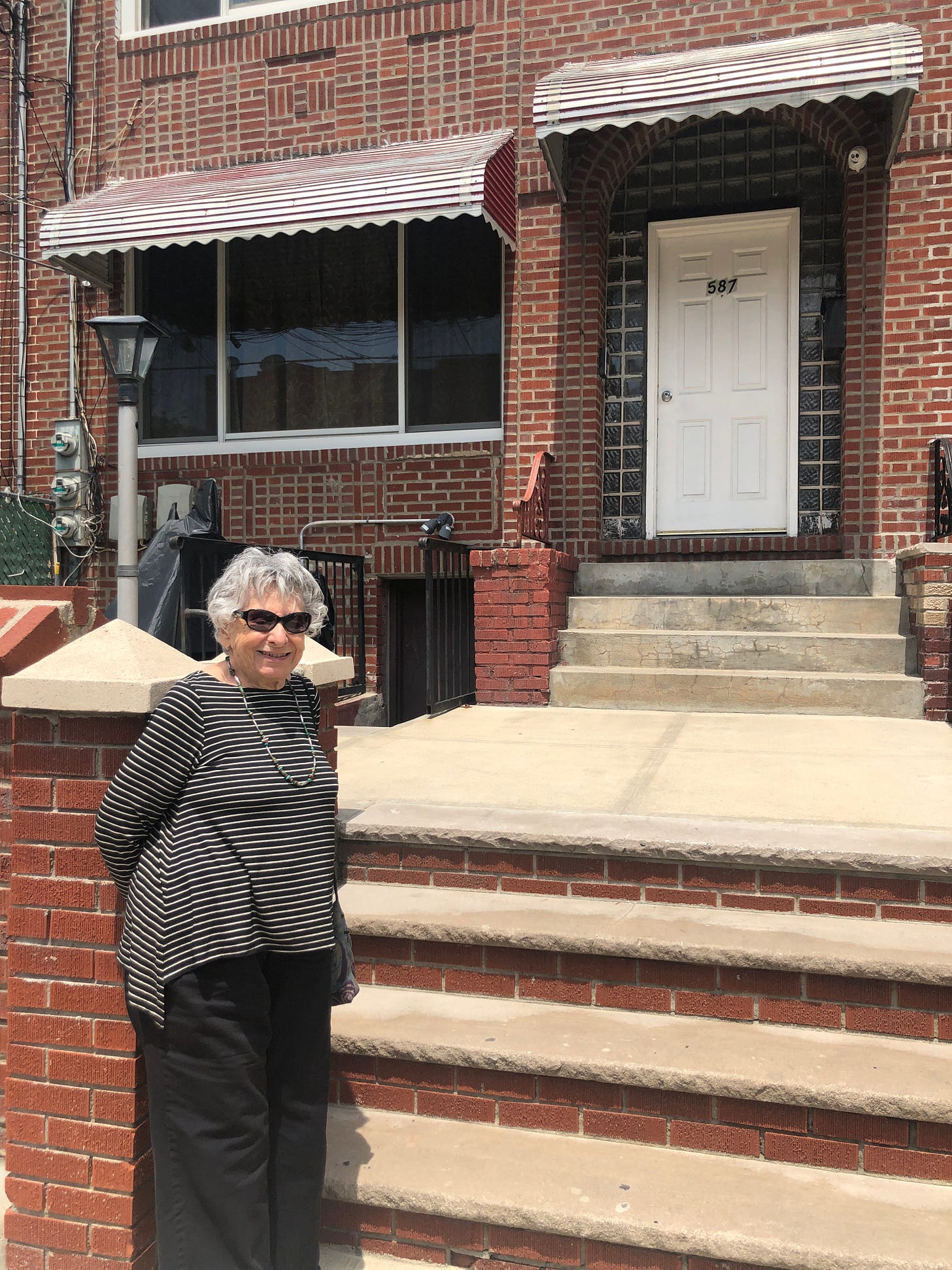My grandma in sunglasses and a stripey shirt, in front of a brownstone in Brooklyn.