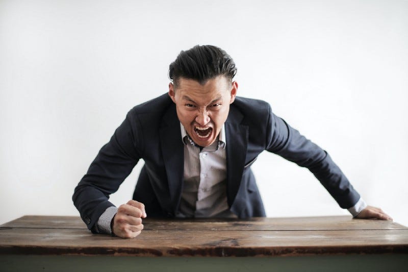 A man in a suit pounding a table and yelling angrily