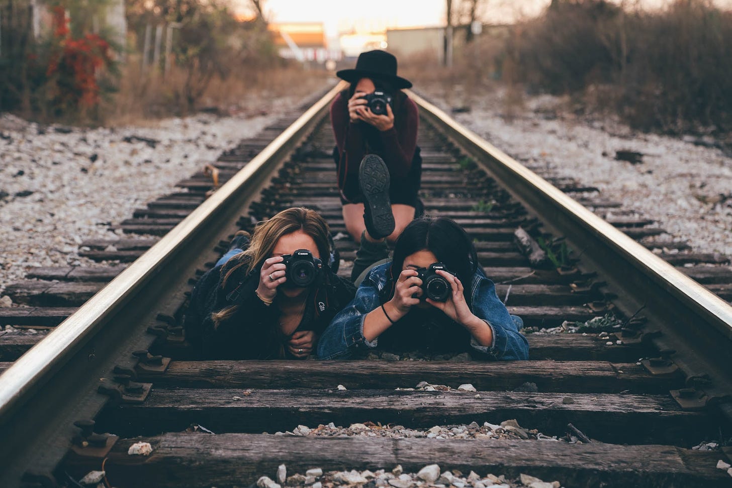 Three woman lie on train tracks pointing their cameras at the viewer