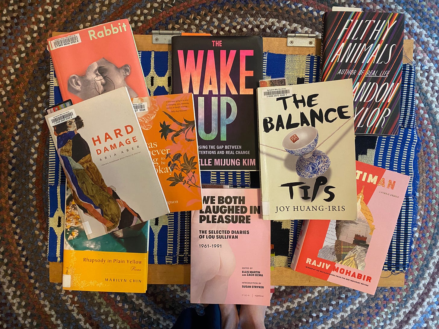 Books arranged messily on a rectangular coffee table. They include: Hard Damage, Rhapsody in Plain Yellow, It Was Never Going to Be Okay, Little Rabbit, The Balance Tips, Filthy Animals, Antiman, The Wake Up, and We Both Laughed in Pleasure.