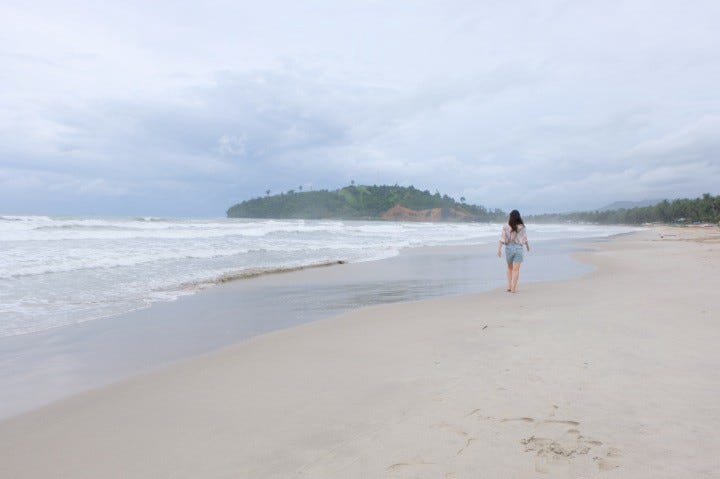 A girl walking by the shore on a white sand beach