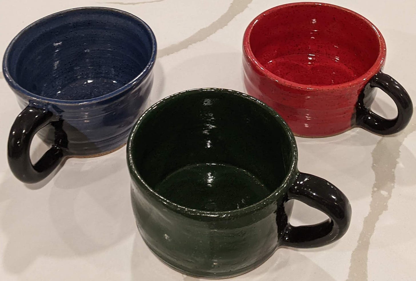 Three mugs, one dark blue, one dark green, one deep red, all three with black handles