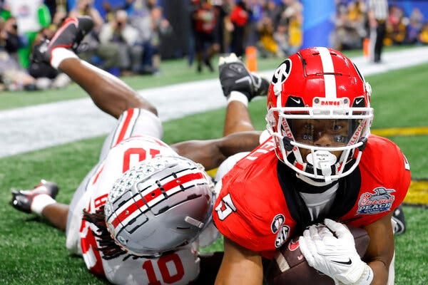 Georgia receiver Adonai Mitchell cradling the ball in his arms while making a catch near the ground in the end zone with an Ohio State defender draped on him.