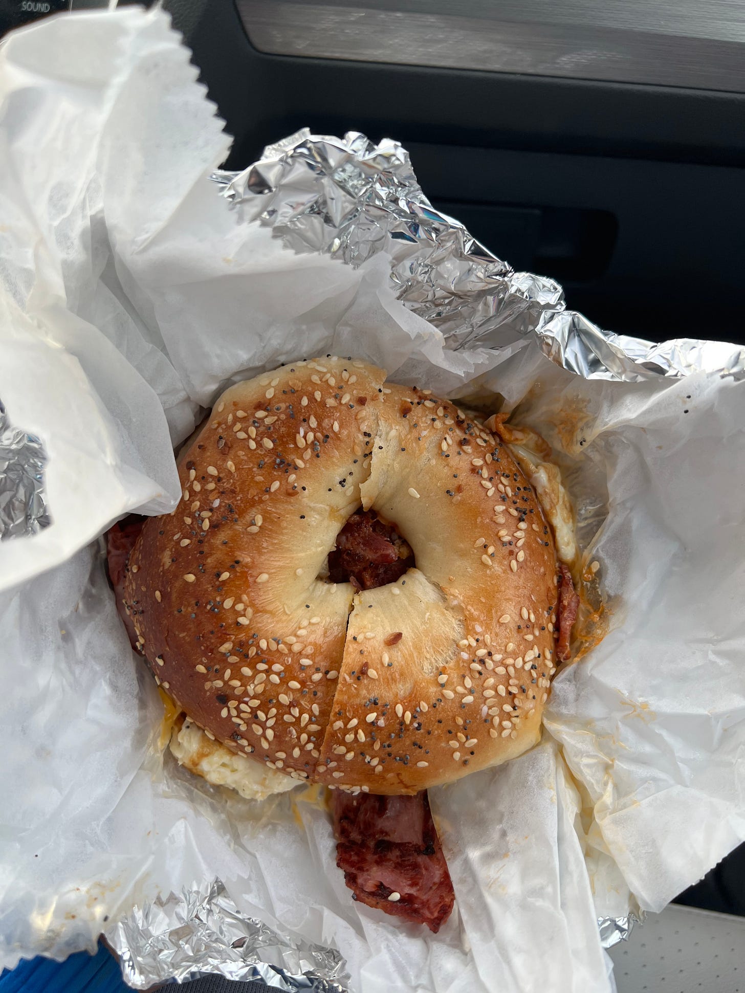 A top down view of a bagel sitting in foil wrapping. The bagel is an everything bagel with turkey bacon, egg white, and cheese. It is perfectly crispy on the outside.
