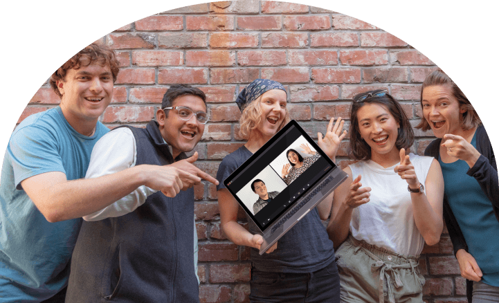 The Multitudes software development  team posing in-front of a brick wall with one holding a laptop where two team members appear via video chat."