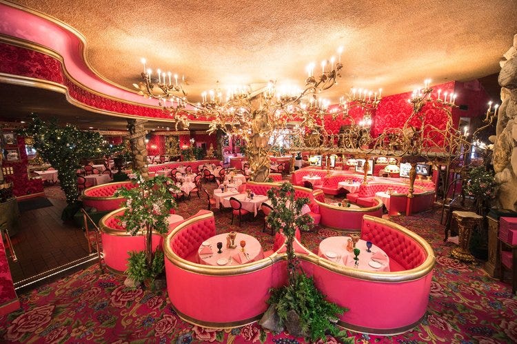 a photo of the steakhouse at the madonna inn. it has lots of bright pink booths, gold chandeliers, and a pink carpet with pink roses