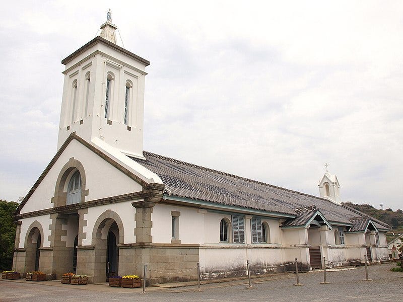 White stucco church with tile roof and stone trim.