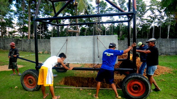 A group of people loading a concrete 'grave liner' into the ground. The casket would then be placed inside.