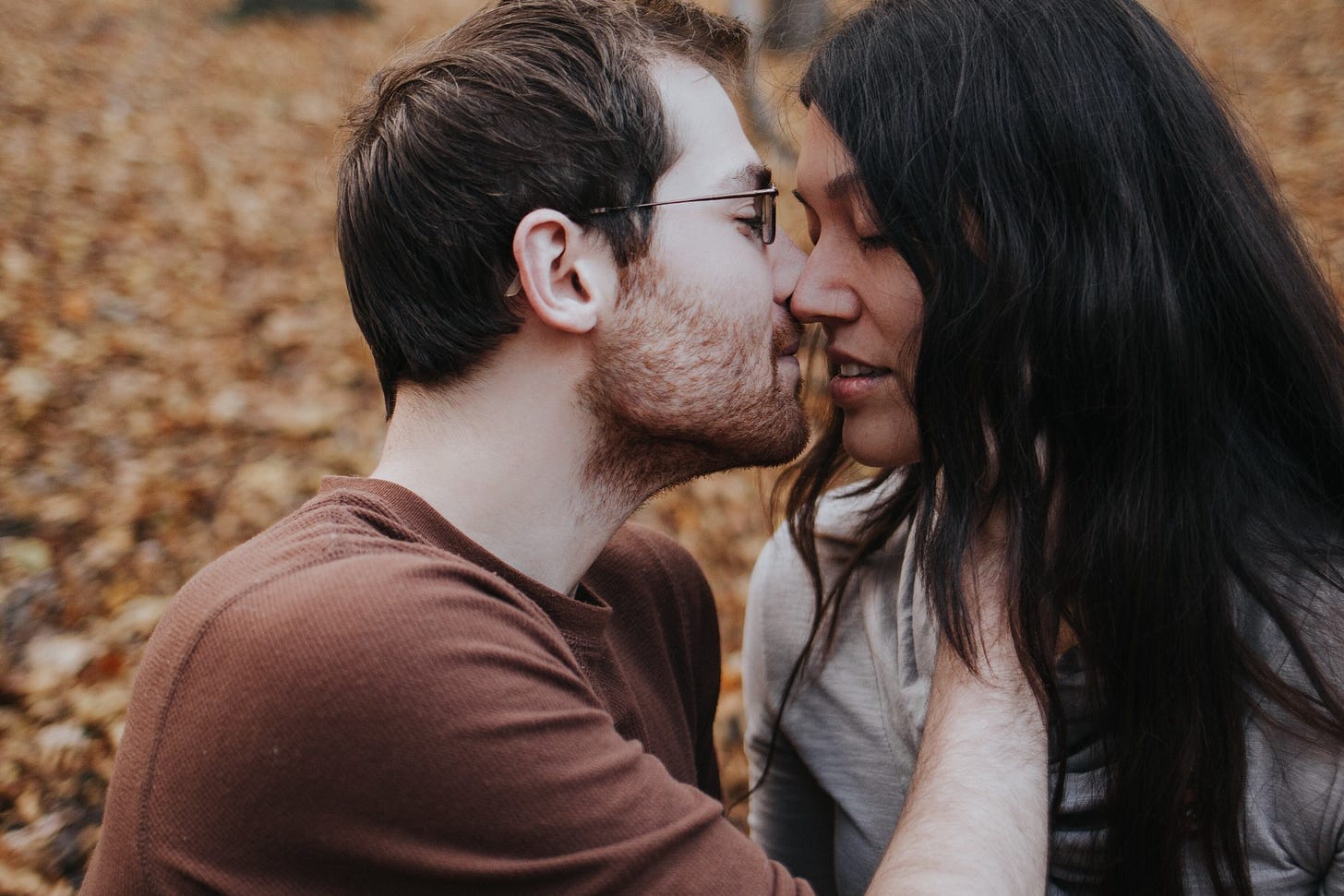 A couple embraces in a leafy park.