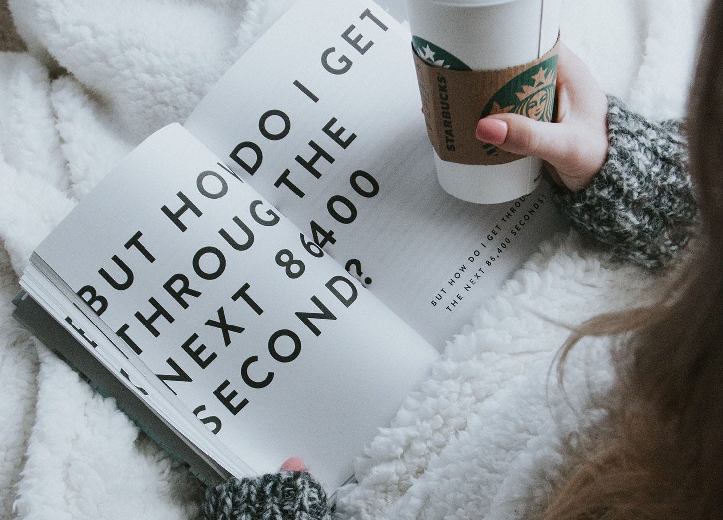 woman holding takeout coffee and reading a book that says in large print, "how to get through the next 86400 seconds."