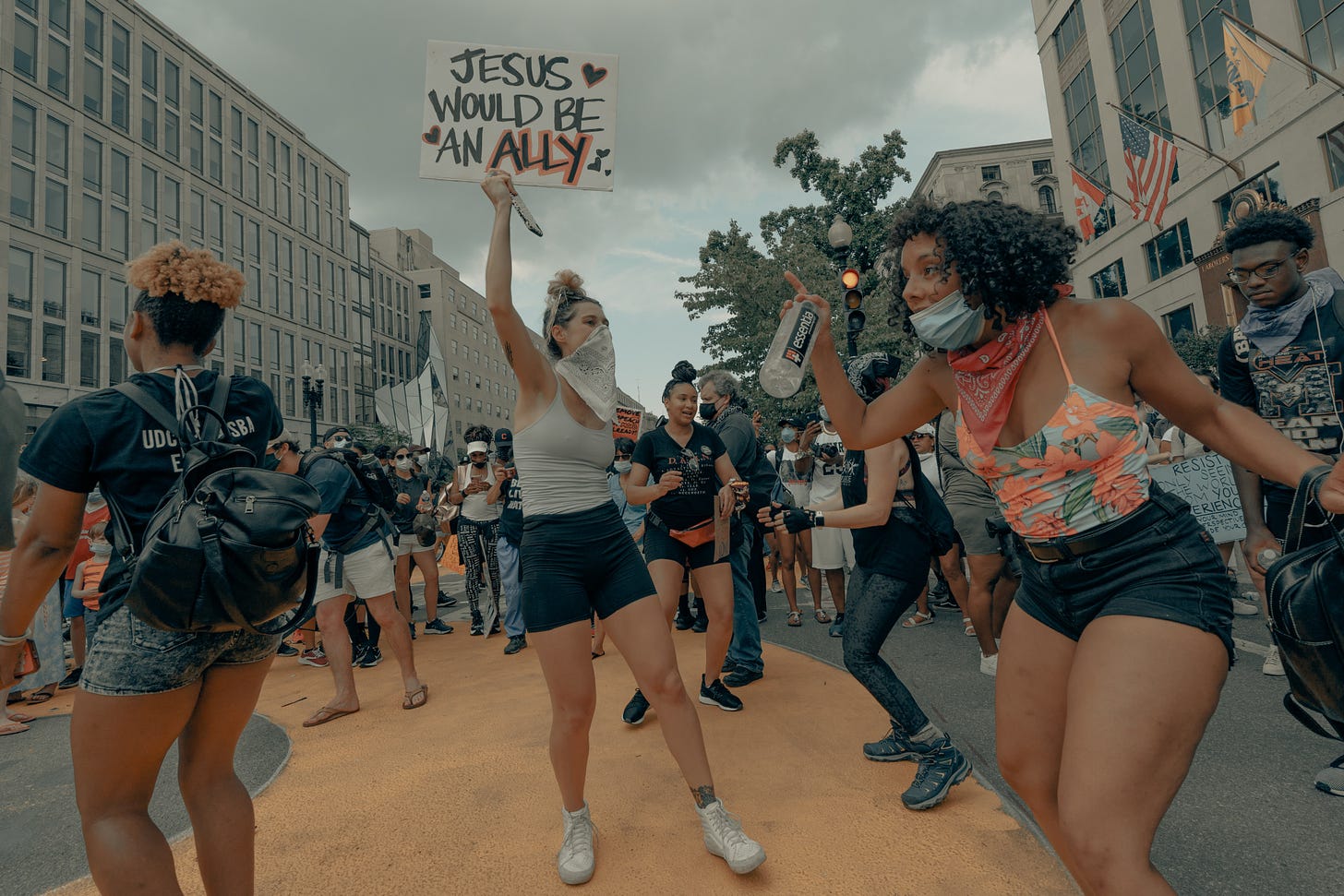 young people dancing at a protest, one is holding a sign that says "Jesus would be an ally"